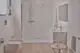 Heller, moderner Badezimmerbereich mit Dusche, Waschbecken und WC. Ideal Standard Brausethermostat ist sichtbar im Duschbereich. Minimalistische Ausstattung mit Holzfußboden.